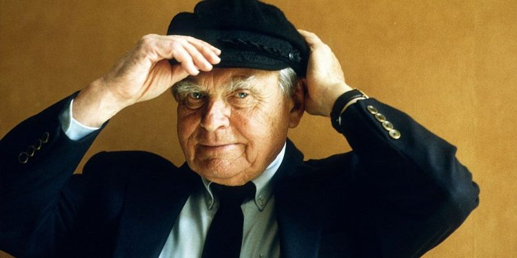 Na zdjęciu znajduje się Czesław Miłosz, który ma ubraną czapkę i trzyma ją rękoma