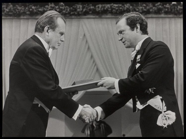 Na zdjęciu znajduje się Czesław Miłosz, który odbiera swoją nagrodę Nobla i ściska rękę wręczającej mu osobie.