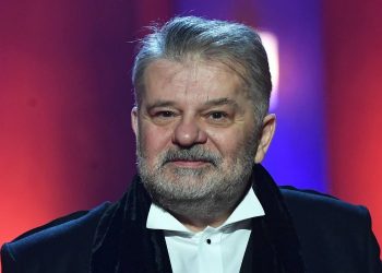 Na zdjęciu znajduje się Krzysztof Globisz ubrany w koszulę i płaszcz