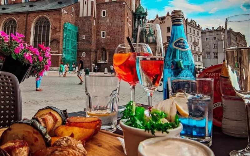 Zdjęcie przedstawia jedzenie na stole w ogródku restauracji The Piano Rouge w Krakowie z widokiem na Bazylikę Mariacką