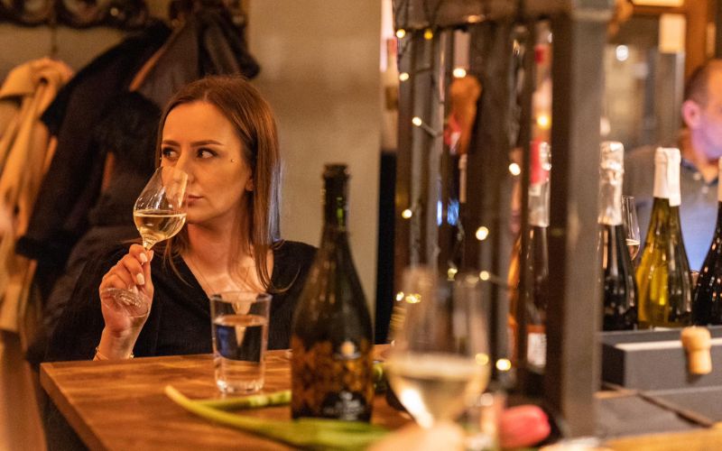 Zdjęcie przedstawia kobietę, która wącha wino znajdujące się w kieliszku