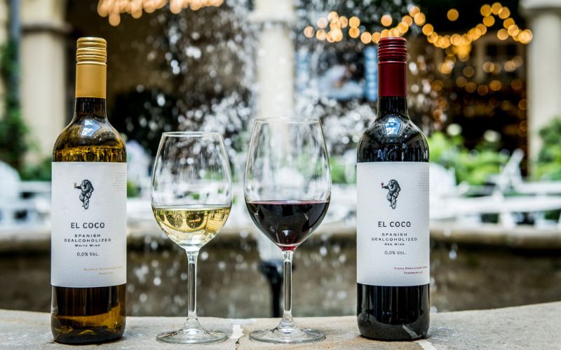 Zdjęcie przedstawia dwa kieliszki wina z inną zawartością. W jednym znajduje się białe wino, w drugim czerwone. Obok kieliszków stoją butelki wina.