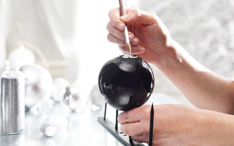 Zdjęcie przedstawia proces malowania ręcznego szklanej bombki choinkowej