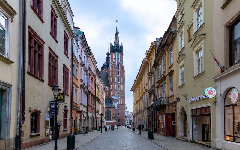 Zdjęcie przedstawia ulicę na rynku w Krakowie, gdzie w oddali widać Bazylikę Mariacką