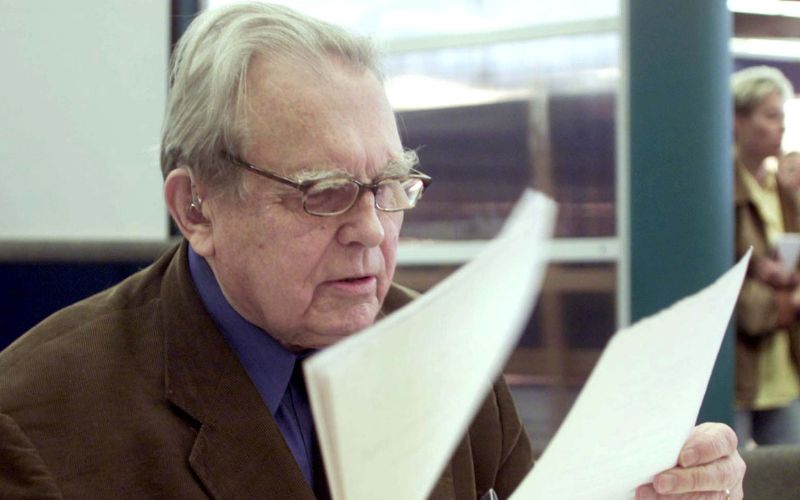 Zdjęcie przedstawia Czesława Miłosza, który wertuje kartki w dłoni