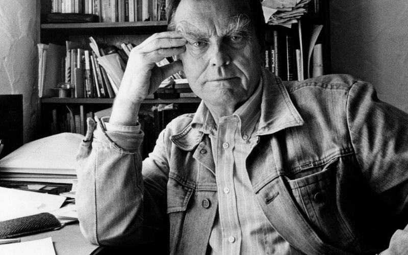 Zdjęcie przedstawia Czesława Miłosza przy biurku, który podtrzymuje jedną ręką swoją twarz