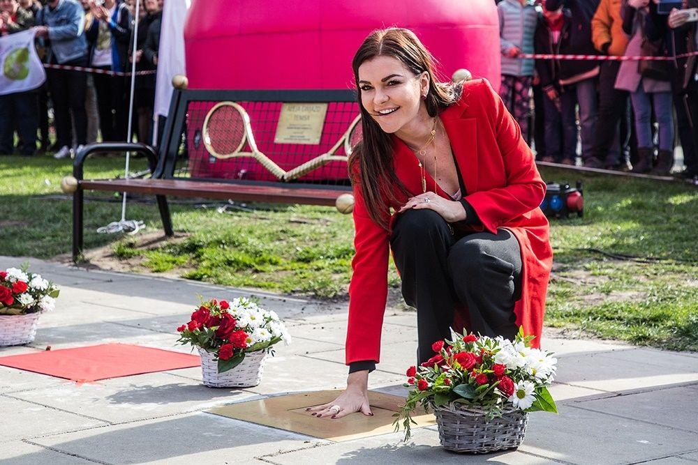 Zdjęcie przedstawia Agnieszką Radwańską, która kuca przy Aleji Sławy i dopasowuje swoją dłoń