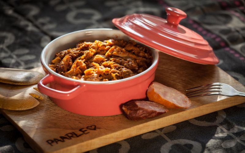 Zdjęcie przedstawia bigos w garnku żeliwnym, obok 2 kromki chleba