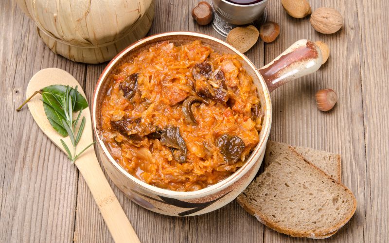 Zdjęcie przedstawia bigos w naczyniu, obok kromka chleba