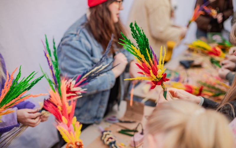 Zdjęcie przedstawia wykonywanie drzewek z kolorowych bazi na kiermaszu wielkanocnym