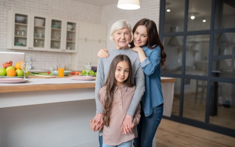 Zdjęcie przedstawia emerytkę z córką i wnuczką, które się obejmują