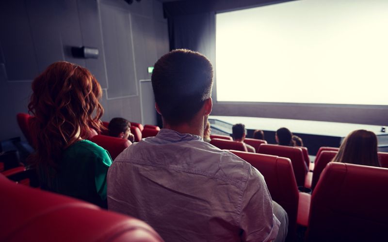 Zdjęcie przedstawia mężczyznę siedzącego w sali kinowej
