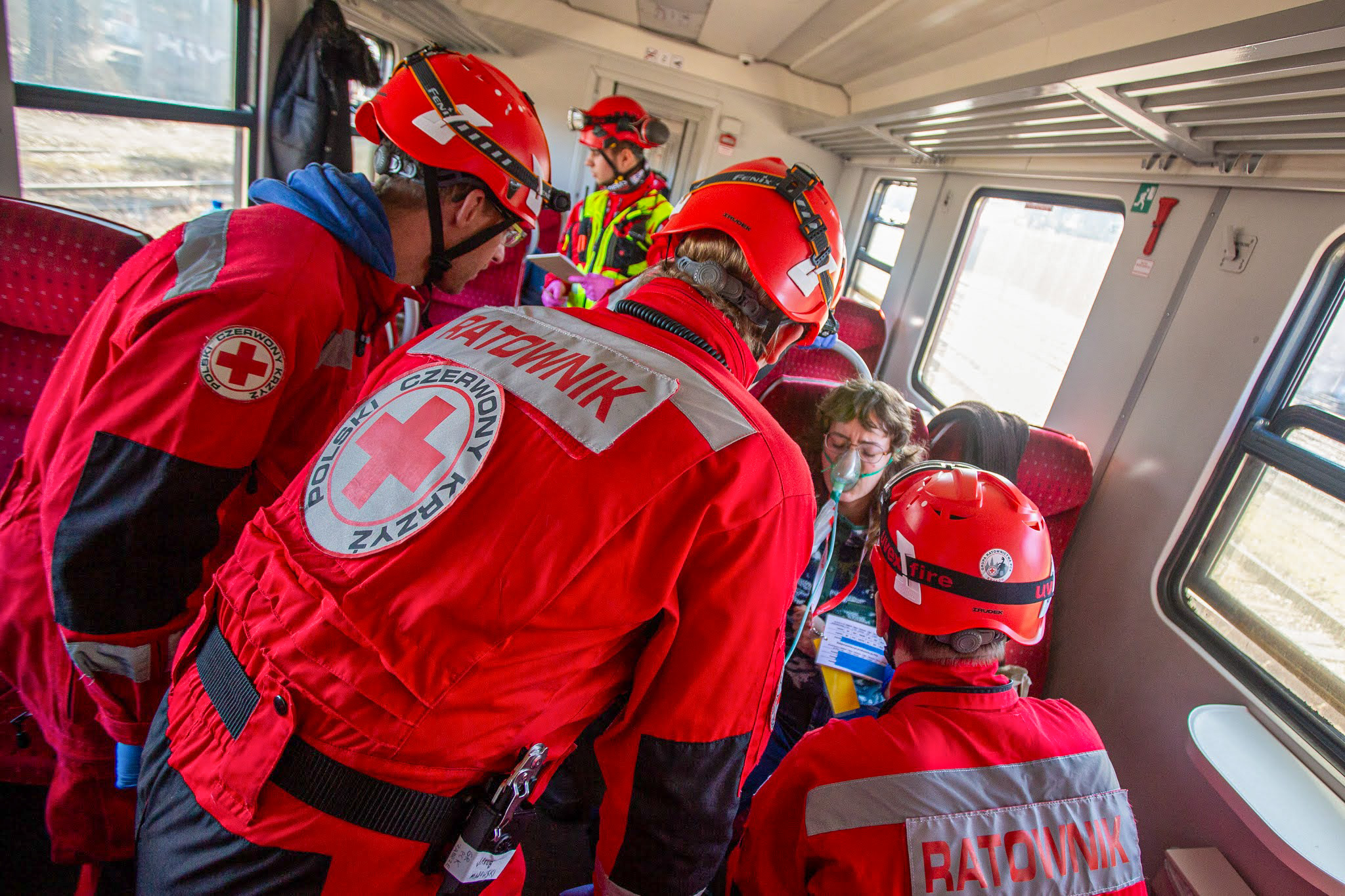 Zdjęcie przedstawia ratowników w wagonie kolejowym, którzy udzielają pomocy poszkodowanej