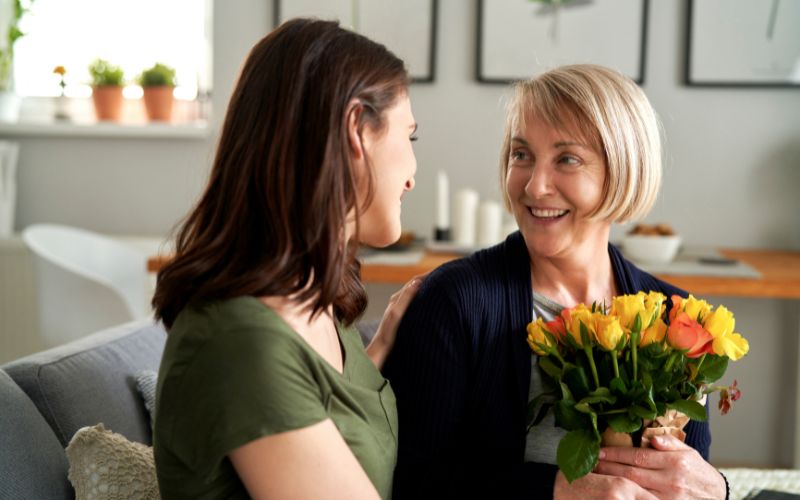 Zdjęcie przedstawia synową, która podaje kwiaty teściowej