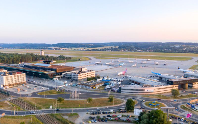 Zdjęcie przedstawia budynek i plac Kraków Airport przy zachodzie słońca wykonany z lotu ptaka
