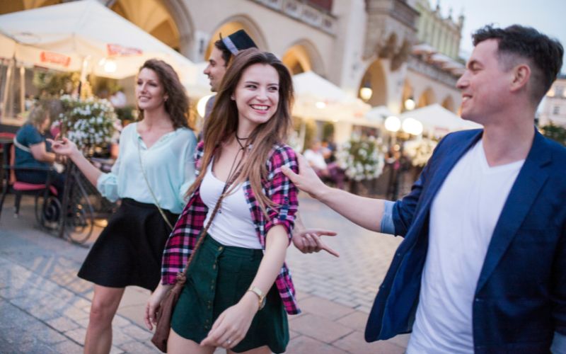 Zdjęcie przedstawia 3 osoby spacerujące po rynku w Krakowie